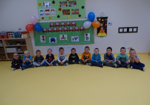 Chłopcy siedzą na podłodze przed tablicą z napisem Dzień Chłopaka